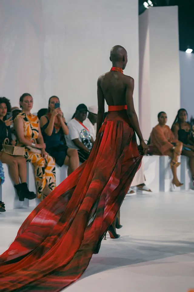 Un mannequin en longue robe rouge sur le podium, vu de dos