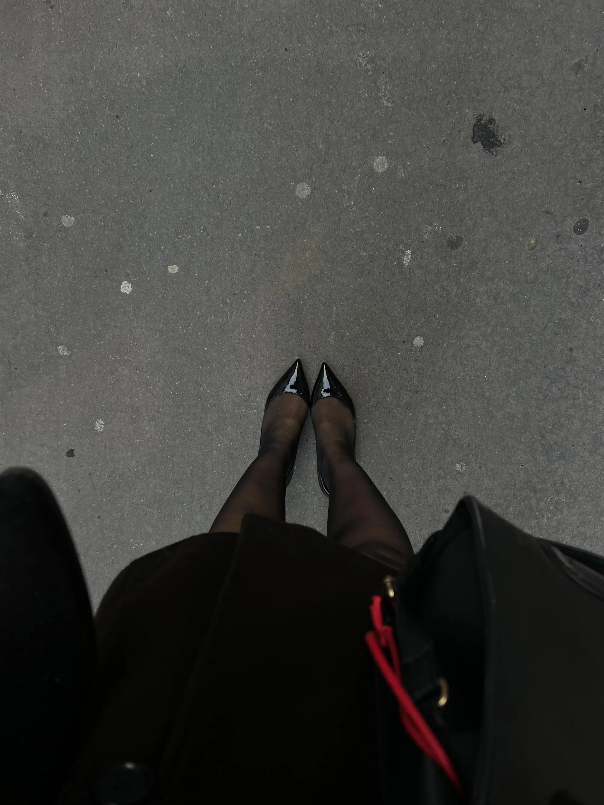 Des escarpins noirs et un sac noir sur le trottoir, vus d’en haut