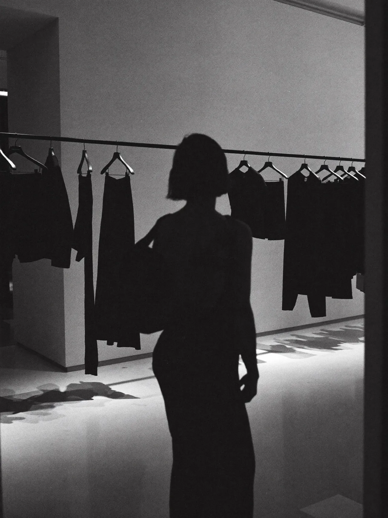 Une silhouette près d’un portant de vêtements noirs dans un showroom blanc