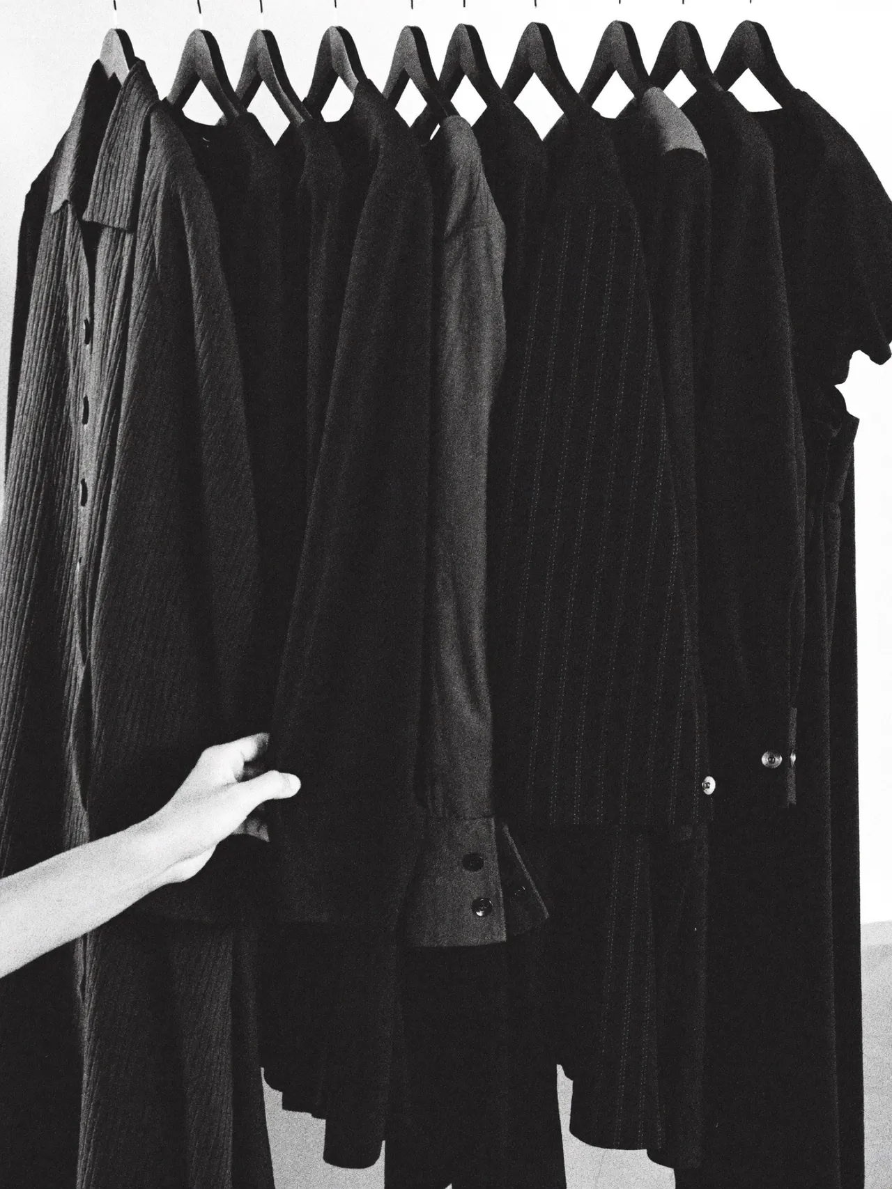 Une main saisit des vêtements noirs sur des cintres