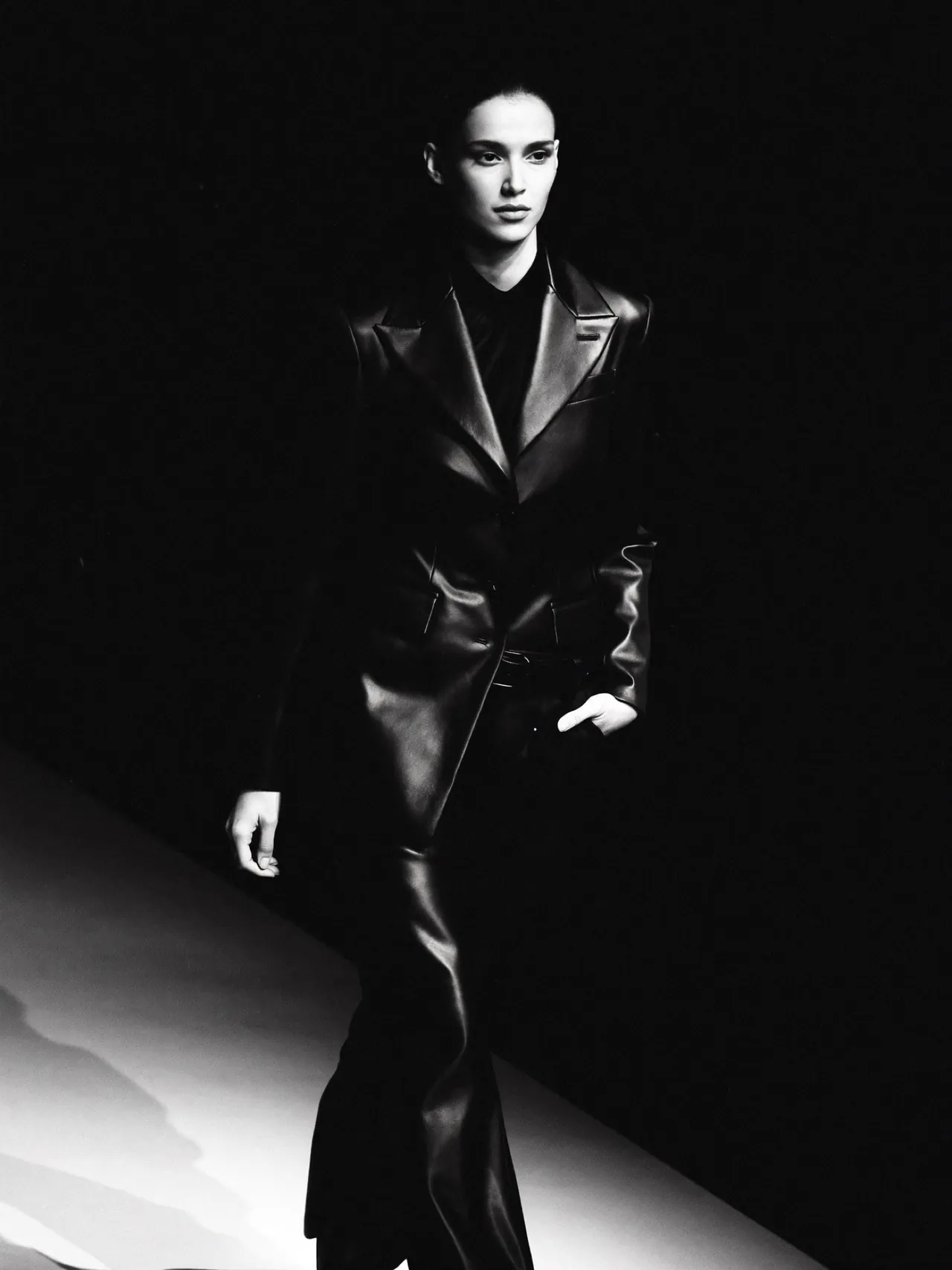Un mannequin en manteau de cuir noir avance sous un projecteur
